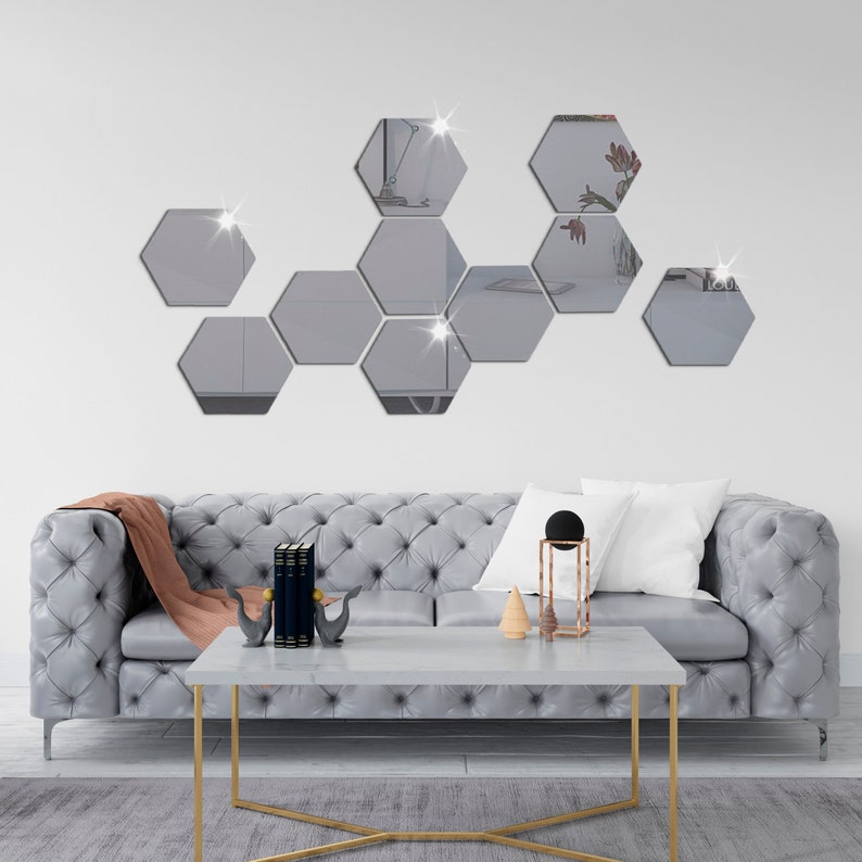 May include: A set of eight hexagonal mirrors in a geometric pattern on a white wall above a gray tufted sofa with a coffee table and decorative objects.
