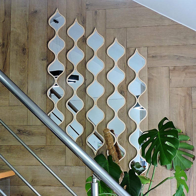 May include: Five decorative wall mirrors with a unique, flowing design. Each mirror has a light wood frame and a series of connected, curved shapes. The mirrors are mounted on a wooden wall, creating a stylish and artistic display.