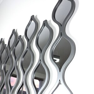 K&ouml;nnte beinhalten: Ein Wandspiegel mit modernem Design mit mehreren &uuml;berlappenden, wellenf&ouml;rmigen Formen in silberner Ausf&uuml;hrung.
