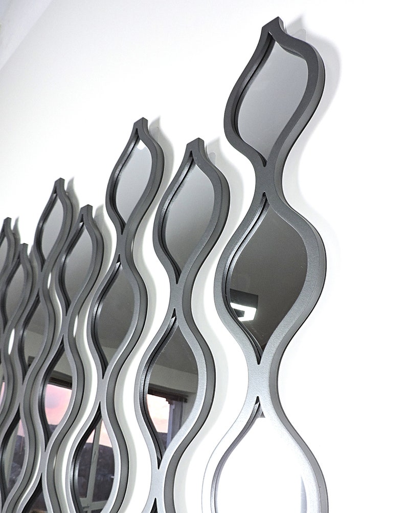 K&ouml;nnte beinhalten: Ein Wandspiegel mit modernem Design mit mehreren &uuml;berlappenden, wellenf&ouml;rmigen Formen in silberner Ausf&uuml;hrung.