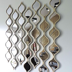 May include: A set of decorative wall mirrors with a unique, flowing design. Each mirror is framed in a light wood color and features an elongated, teardrop shape. The mirrors are arranged in vertical, wavy patterns, creating a modern aesthetic.