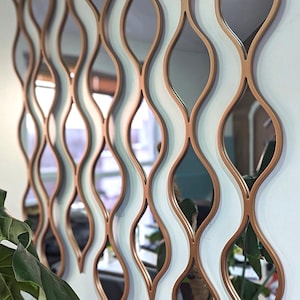 Op de afbeelding: Een decoratieve wandspiegel met een uniek ontwerp met meerdere overlappende, traanvormige spiegels in een koperen afwerking.