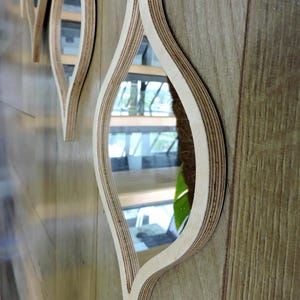 May include: Decorative wall mirrors with a unique leaf-like design. The mirrors are framed with layered light-colored wood, creating a three-dimensional effect. The mirrors are mounted on a wooden wall.