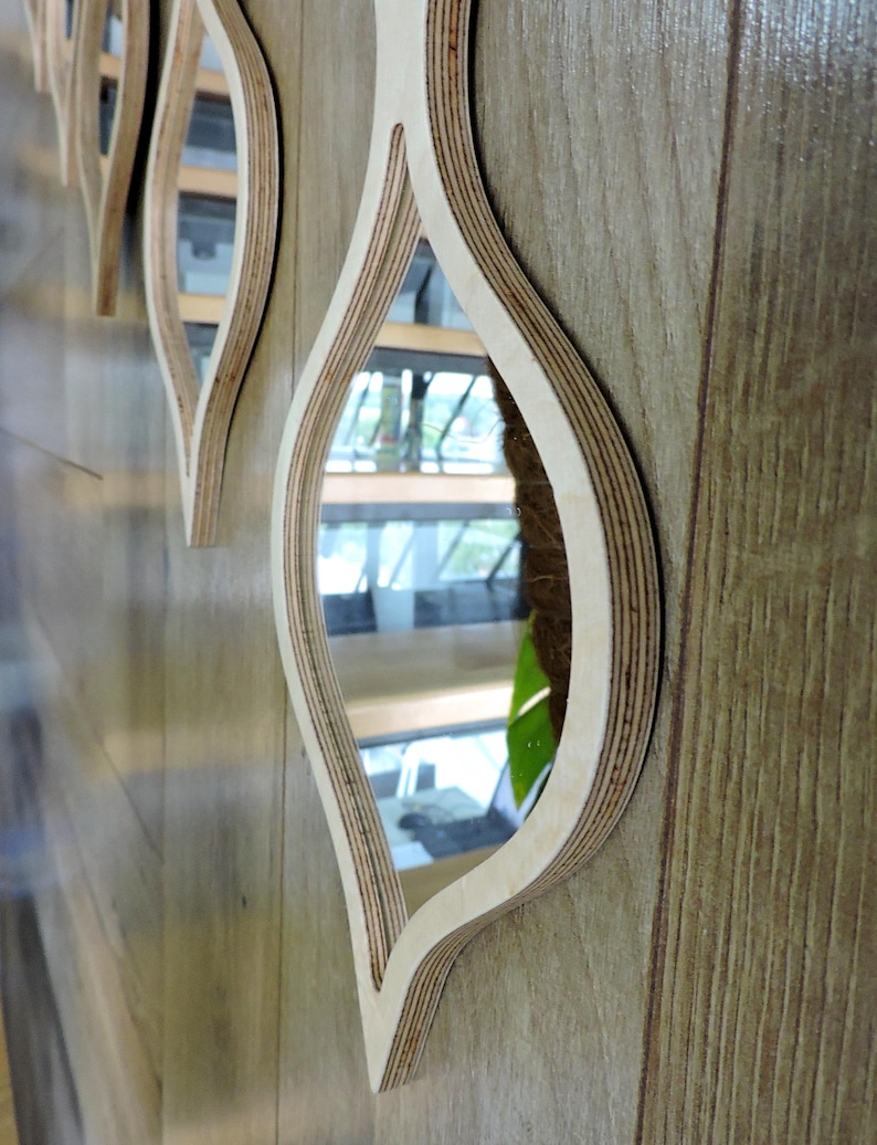 May include: Decorative wall mirrors with a unique leaf-like design. The mirrors are framed with layered light-colored wood, creating a three-dimensional effect. The mirrors are mounted on a wooden wall.