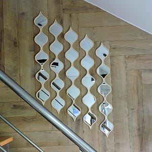May include: Five decorative mirrors with a wavy, elongated design are mounted on a wooden wall. Each mirror has a light-colored wooden frame and a series of oval-shaped reflective surfaces. The mirrors are arranged vertically, creating a unique wall art installation.