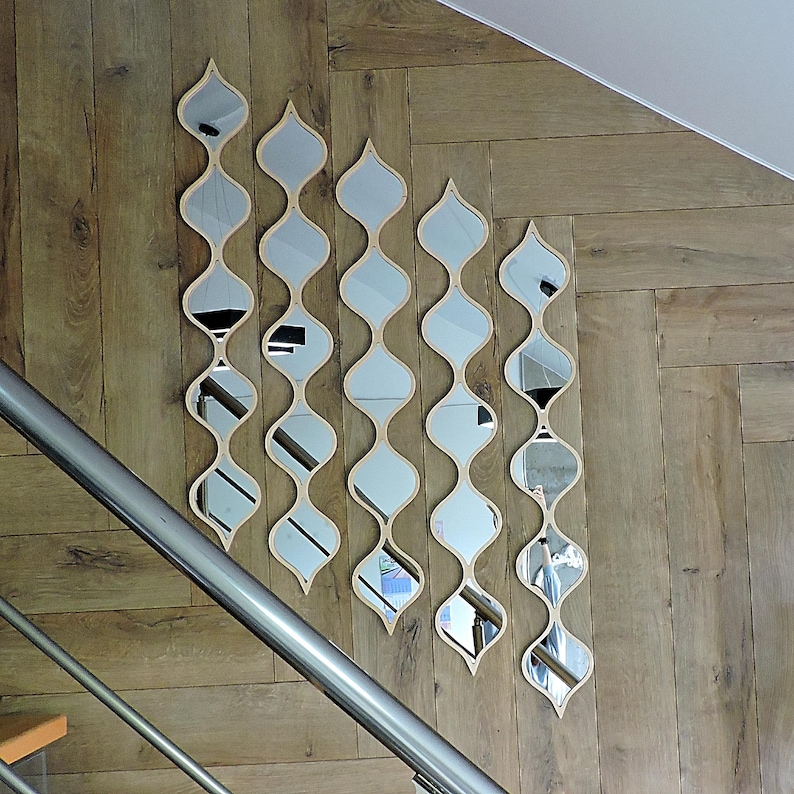 May include: Five decorative mirrors with a wavy, elongated design are mounted on a wooden wall. Each mirror has a light-colored wooden frame and a series of oval-shaped reflective surfaces. The mirrors are arranged vertically, creating a unique wall art installation.