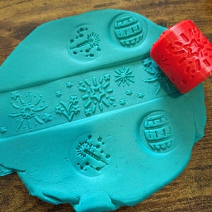 May include: A teal blue play dough with various firework designs pressed into it. A red rolling pin with a firework design is also shown.