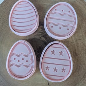 May include: Four pink plastic Easter egg cookie cutters with different designs. The designs include stripes, wavy lines, stars, and dots.