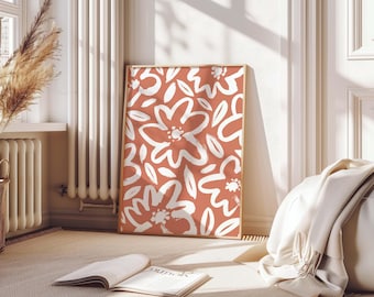 May include: A framed art print featuring a terracotta background with white floral designs. The artwork is displayed on a beige carpet, leaning against a white wall. The room has a neutral color palette, with a window and radiator visible.