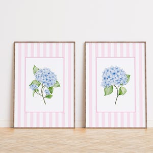 May include: Two framed prints with a pink and white striped background. Each print features a watercolor illustration of a blue hydrangea flower.