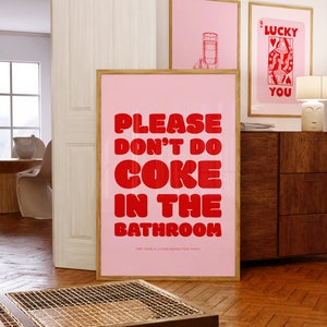 Könnte beinhalten: Gerahmte rosa Poster mit humorvollen Texten und Illustrationen. Das Hauptposter zeigt in roter Schrift: "PLEASE DON'T DO COKE IN THE BATHROOM". Weitere Poster zeigen eine Spielkarte und eine Getränkeillustration.
