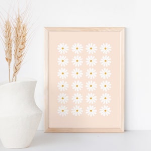 May include: A framed print with a pattern of white daisies with yellow centers on a light pink background.