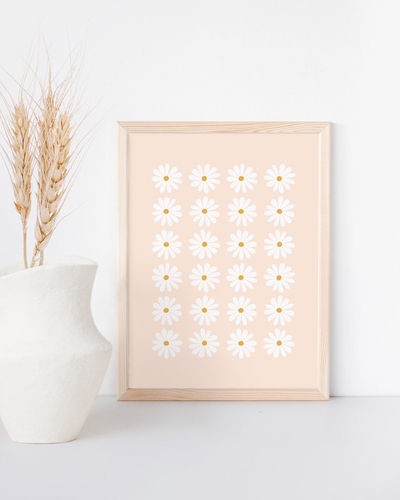 May include: A framed print with a pattern of white daisies with yellow centers on a light pink background.