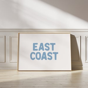 Puede incluir: Una impresión enmarcada con el texto "EAST COAST" en azul claro sobre un fondo blanco.
