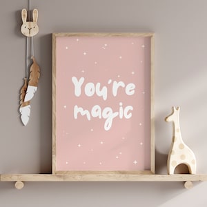 May include: A pink framed print with white stars and the text "You're magic" on a light brown shelf with a wooden bunny and giraffe figurine.