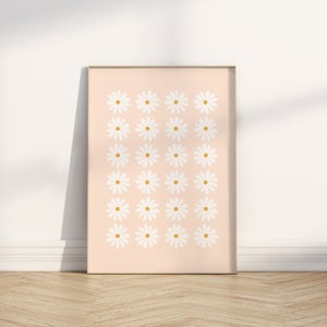 May include: A framed print with a pattern of white daisies with yellow centers on a light pink background.
