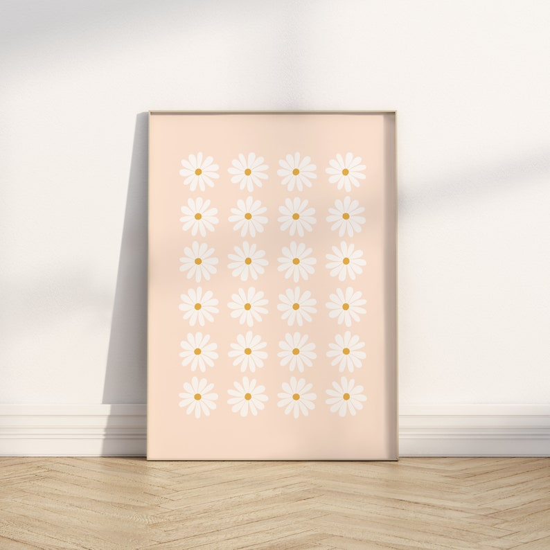 May include: A framed print with a pattern of white daisies with yellow centers on a light pink background.