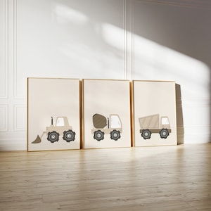 May include: Set of three framed prints featuring illustrations of construction vehicles. The prints are beige with brown details and are displayed on a white wall.