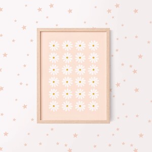 May include: A framed print with a pink background and a grid of white daisies with yellow centers. The frame is light wood and the print is surrounded by a white background with scattered pink stars.