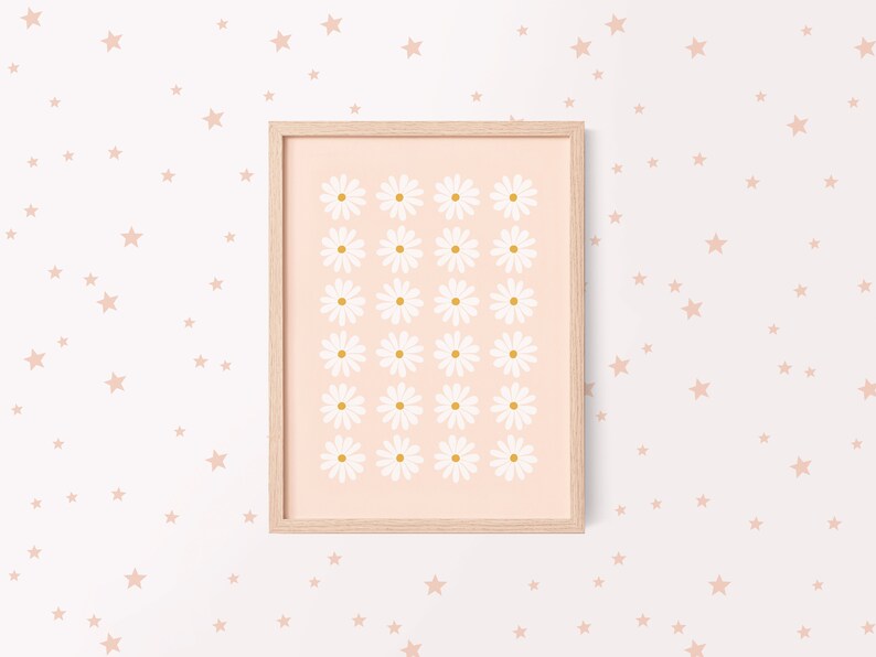 May include: A framed print with a pink background and a grid of white daisies with yellow centers. The frame is light wood and the print is surrounded by a white background with scattered pink stars.