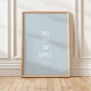 Könnte beinhalten: Ein gerahmter Druck mit hellblauem Hintergrund und weißen Sternen. Der Druck sagt "You are so loved" in weißer Schrift.