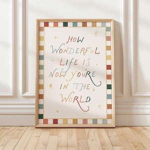May include: A framed art print with the words "HOW WONDERFUL LIFE IS NOW YOU'RE IN THE WORLD" in colourful script. The print has a cream background with colourful stars and a border of alternating coloured squares. The frame is a light wood colour.