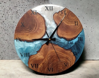 May include: A round wooden clock face with Roman numerals and black hands. The clock face is made of wood with a blue and white epoxy resin inlay. The clock face is approximately 12 inches in diameter.