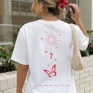 K&ouml;nnte beinhalten: Wei&szlig;es T-Shirt mit roter Grafik auf dem R&uuml;cken, die eine Sonne, Schmetterlinge, die Zahl 7 und den Schriftzug "I'LL FOLLOW YOU INTO THE SUN" zeigt. Das Shirt hat kurze &Auml;rmel und eine lockere Passform.