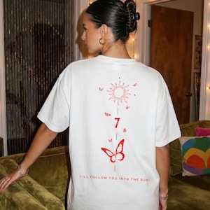 K&ouml;nnte beinhalten: Wei&szlig;es T-Shirt mit roter Grafik auf dem R&uuml;cken. Die Grafik zeigt eine Sonne, Schmetterlinge, die Zahl 7 und den Text "I'LL FOLLOW YOU INTO THE SUN". Das Shirt hat eine lockere Passform.