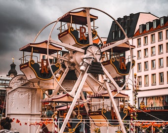 May include: A white and red Ferris wheel with ornate carriages, set against a cloudy sky. The Ferris wheel is decorated with gold accents and floral details. The Ferris wheel is in front of a building with a black roof.
