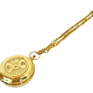 Könnte beinhalten: Eine goldfarbene Taschenuhr mit Kette. Das Zifferblatt der Uhr zeigt ein Kalendarium mit Text und einem dekorativen Design. Die Kette ist ebenfalls goldfarben und an der Uhr befestigt.