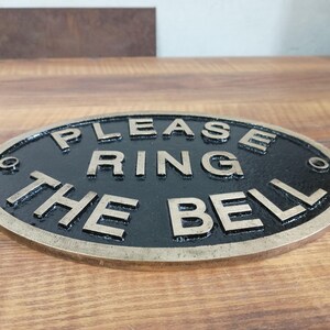 May include: An oval-shaped metal sign with a black background and raised brass-coloured lettering that reads "PLEASE RING THE BELL". The sign features a metallic border and four small circular holes for mounting, one located at each corner. yacht cabin plaque, yacht decor, yacht interior decor, yacht entrance sign, yacht owner gift, yacht gift idea, captain door sign, captain door plaque, captain sign, captain plaque, captain cabin sign, captain cabin plaque, captain cabin decor,