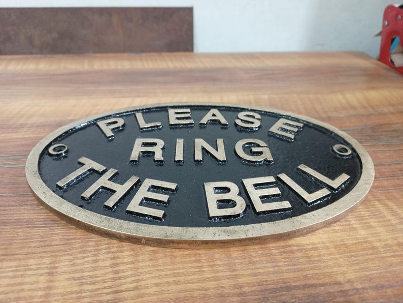 May include: An oval-shaped metal sign with a black background and raised brass-coloured lettering that reads "PLEASE RING THE BELL". The sign features a metallic border and four small circular holes for mounting, one located at each corner. yacht cabin plaque, yacht decor, yacht interior decor, yacht entrance sign, yacht owner gift, yacht gift idea, captain door sign, captain door plaque, captain sign, captain plaque, captain cabin sign, captain cabin plaque, captain cabin decor,