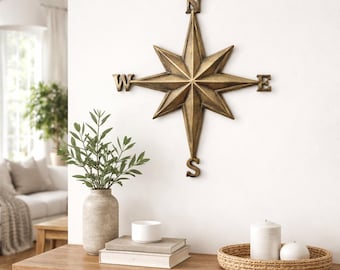 Op de afbeelding: Een wandsculptuur in de vorm van een windroos met een metallic bronzen afwerking. Het stervormige ontwerp heeft vier langwerpige punten met de letters N, S, E en W aan de uiteinden van de windstreken om noord, zuid, oost en west aan te duiden.