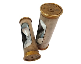 May include: Two antique hourglasses with brass accents and tan leather casing. The glass vials contain white sand. The hourglasses are cylindrical and have a vintage aesthetic. The top and bottom of the hourglasses are brass with engraved details.