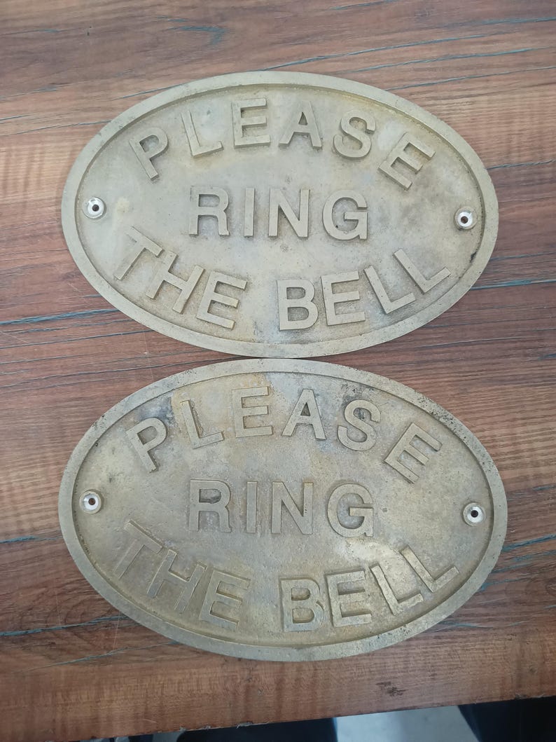 May include: Two oval-shaped brass signs with a weathered finish. Each sign features raised lettering that reads "PLEASE RING THE BELL" in a clear, sans-serif font. There are two small circular mounting holes on the left and right sides of each sign. coastal home decor, coastal entry sign, coastal decor, beach house decor, seaside decor, ocean decor, sea decor, ship decor, ship door sign, ship door plaque, ship cabin decor, maritime gift, nautical gift, nautical gift idea,
