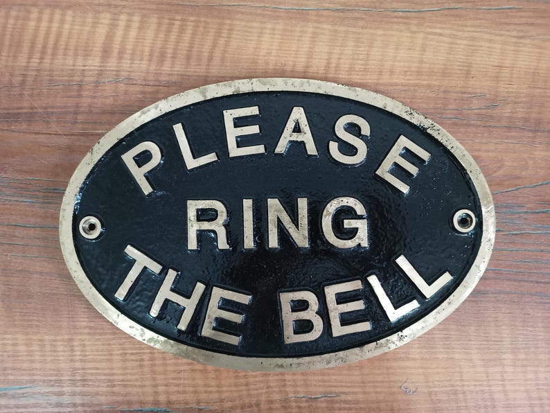 May include: An oval-shaped metal sign with a black background and a brass-coloured border. The sign features raised, metallic lettering that reads "PLEASE RING THE BELL" in three lines. There are two circular mounting holes on the left and right sides. boat cabin plaque, boat decor, boat interior decor, boat entrance sign, boat owner gift, boat gift idea, yacht door sign, yacht door plaque, yacht entry sign, yacht entry plaque, yacht wall plaque, yacht wall decor, yacht cabin sign,