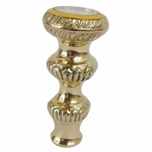 May include: A decorative, gold-coloured bottle stopper with an ornate, layered design. The stopper features a detailed pattern and a silver-coloured top with a gold band. The design is symmetrical and elegant.
