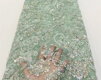 May include: A pale green beaded lace fabric with a floral pattern. The fabric is decorated with sequins and pearls.