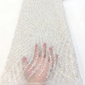 May include: White beaded lace fabric with a delicate pearl design. The fabric is sheer and has a soft, flowing texture.