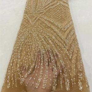 Peut inclure: Tissu perlé doré avec une finition chatoyante et irisée. Le tissu présente un motif répétitif de lignes verticales et un design délicat et fluide. Les perles sont petites et uniformément espacées, créant un aspect luxueux et élégant.