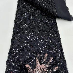 May include: Black sequined fabric with a scale pattern and beaded accents. The fabric is sheer and has a delicate texture.