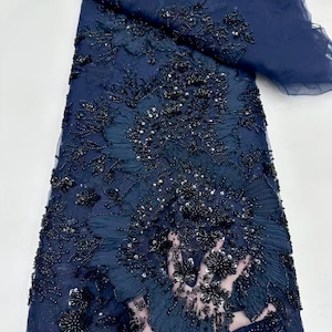 以下が含まれることがあります： 紺色のビーズ付きレース生地で、花柄のデザインです。生地は透き通っていて、繊細な質感です。