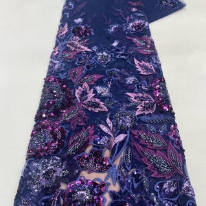 May include: Navy blue lace fabric with floral embroidery. The fabric features intricate designs with purple, pink, and silver sequins. The floral pattern includes leaves and flowers, creating a textured and detailed appearance.