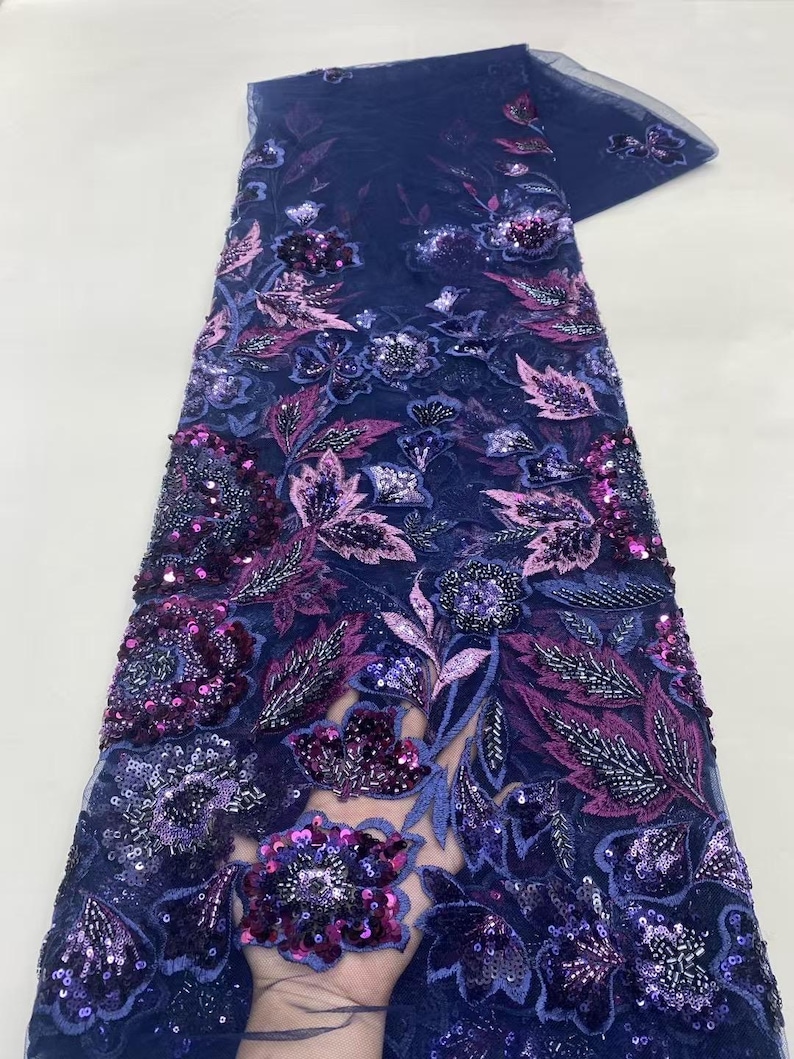May include: Navy blue lace fabric with floral embroidery. The fabric features intricate designs with purple, pink, and silver sequins. The floral pattern includes leaves and flowers, creating a textured and detailed appearance.
