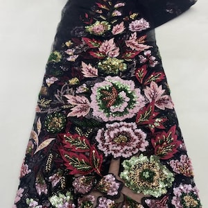 May include: Black fabric with an embroidered floral design. The design features large flowers in shades of pink, green, and red, with gold and green sequins. The fabric is likely intended for use in apparel or decorative projects.