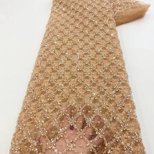 Könnte beinhalten: Ein beigefarbener Perlen-Spitzenstoff mit geometrischem Muster. Der Stoff ist mit Pailletten und Perlen verziert.