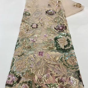May include: Beige lace fabric with intricate floral embroidery. The design features detailed flowers in shades of green, purple, and gold, embellished with sequins. The fabric is suitable for dresses, veils, or other decorative projects.
