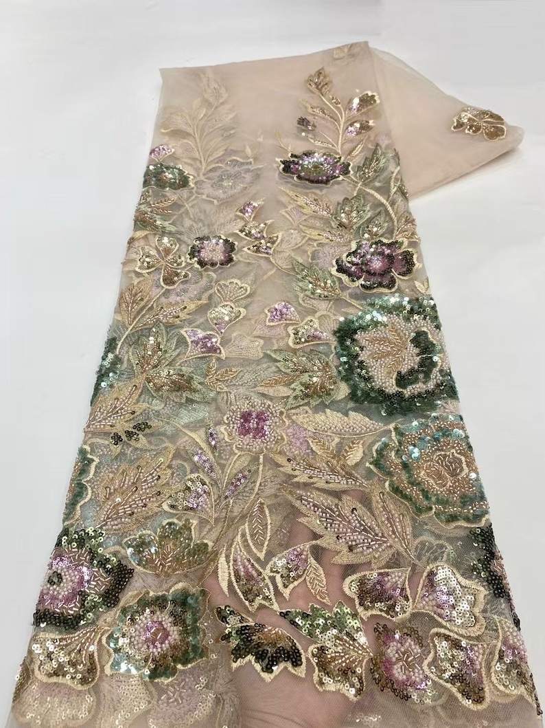May include: Beige lace fabric with intricate floral embroidery. The design features detailed flowers in shades of green, purple, and gold, embellished with sequins. The fabric is suitable for dresses, veils, or other decorative projects.
