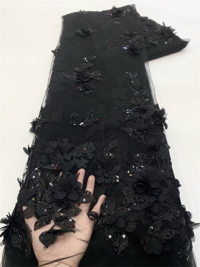 May include: Black floral lace fabric with 3D flowers and sequins. The fabric has a delicate mesh base and is adorned with intricate floral designs. The flowers are made of a soft, textured material and are embellished with sparkling sequins. The fabric is perfect for creating elegant and sophisticated garments.